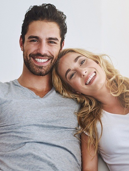 Smiling man and woman sitting together on couch after dental bonding treatment