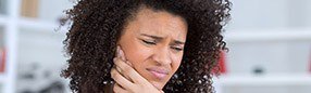Woman holding cheek in pain before emergency dentistry