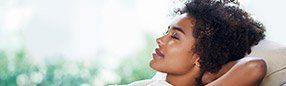 Woman relaxing with hands behind head after sedation dentistry visit